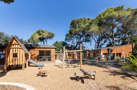 Parque infantil con casita de madera y columpios en Huttopia La Forêt de Janas en Provence-Alpes-Côte d’Azur, Francia.