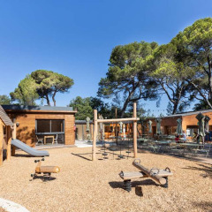 Parque infantil con casita de madera y columpios en Huttopia La Forêt de Janas en Provence-Alpes-Côte d’Azur, Francia.