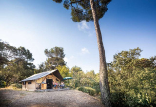 Sfeervolle tent met terras in Huttopia La Forêt de Janas, Provence, omgeven door bomen en natuur.