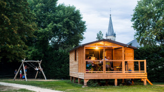 Cabaña de madera Chalet Evasion con personas en el porche y niños jugando en columpios cerca al atardecer.