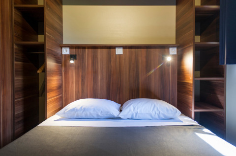 Cama doble cómoda con dos almohadas en una cabaña de madera moderna en Chalet Evasion, Huttopia La Forêt de Janas, Francia.