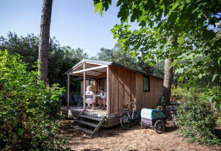 Dos personas descansan en el porche de una cabaña Chalet Evasion en Huttopia La Forêt de Janas, Francia.