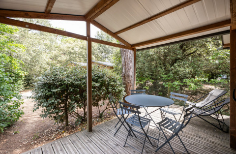 Træterrasse med havebord og stole under overdækning ved Chalet Evasion, Huttopia La Forêt de Janas, Frankrig.