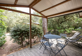 Træterrasse med havebord og stole under overdækning ved Chalet Evasion, Huttopia La Forêt de Janas, Frankrig.
