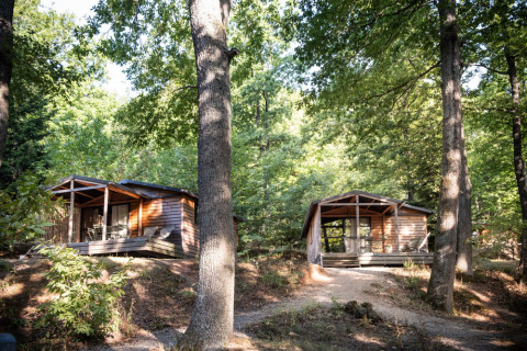 Dos cabañas de madera en el bosque en Chalet Evasion, Huttopia La Forêt de Janas, Francia, entre árboles.