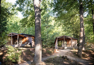 Dos cabañas de madera en el bosque en Chalet Evasion, Huttopia La Forêt de Janas, Francia, entre árboles.
