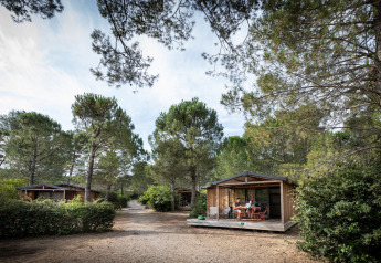Træhytter i skoven ved Chalet Evasion, Huttopia La Forêt de Janas i Frankrig, med folk på terrassen.