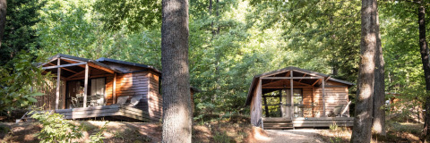 To hyggelige Chalet Evasion-træhytter i skoven ved Huttopia La Forêt de Janas, Frankrig, omgivet af natur.