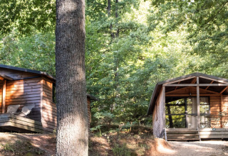 Dos cabañas de madera Chalet Evasion en el bosque de Huttopia La Forêt de Janas, Francia, rodeadas de árboles.