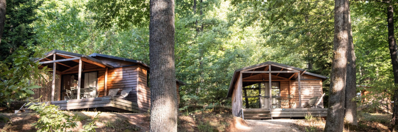Dos cabañas de madera Chalet Evasion en el bosque de Huttopia La Forêt de Janas, Francia, rodeadas de árboles.