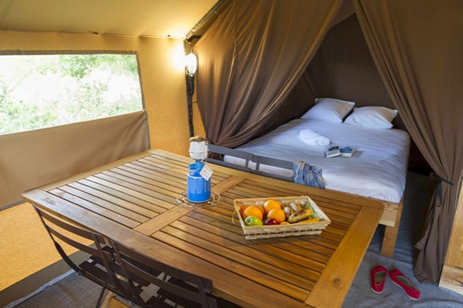 Comfortabele safaritent met tweepersoonsbed, houten tafel, fruitmand en een sfeervolle verlichting.