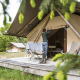 En person åbner en safari teltindgang på en træterrasse i en skov, glamping udendørs i naturen.