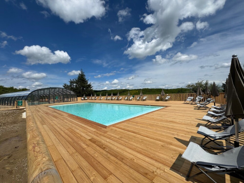 Piscina exterior con terraza de madera y tumbonas bajo cielo azul en Village Huttopia Pays de Condrieu.