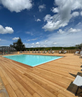 Außenpool mit Holzterrasse und Liegestühlen unter blauem Himmel im Village Huttopia Pays de Condrieu.