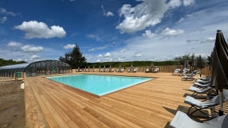 Piscina exterior con terraza de madera y tumbonas bajo cielo azul en Village Huttopia Pays de Condrieu.