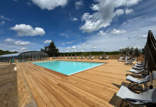 Außenpool mit Holzterrasse und Liegestühlen unter blauem Himmel im Village Huttopia Pays de Condrieu.