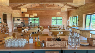 Comedor de madera claro y espacioso con botellas, vasos y vista a la naturaleza a través de las ventanas.
