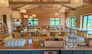 Helles, geräumiges Holzrestaurant mit Glasflaschen, Gläsern und Ölflaschen vor Fensterblick.