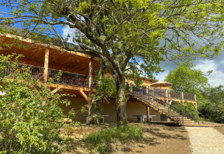 Terrasse extérieure en bois du Village Huttopia Pays de Condrieu entourée d’arbres en Auvergne-Rhône-Alpes.