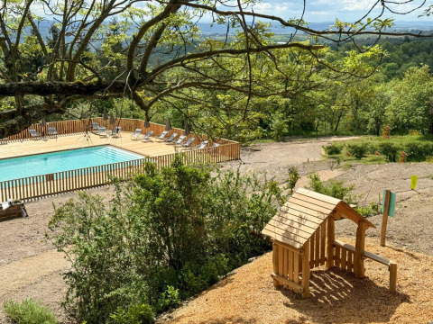 Vista de una piscina y área de juegos rodeadas de árboles en Village Huttopia Pays de Condrieu, Francia.