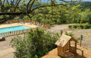 Udsigt over en swimmingpool og legeplads omgivet af træer i ferieparken Village Huttopia Pays de Condrieu.