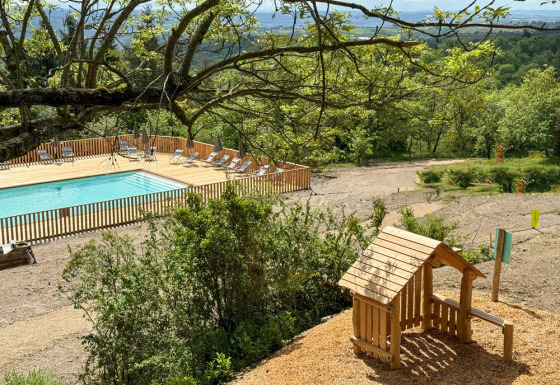 Udsigt over en swimmingpool og legeplads omgivet af træer i ferieparken Village Huttopia Pays de Condrieu.