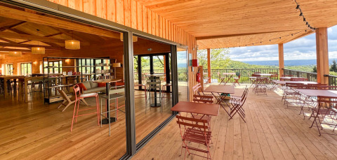 Outdoor and indoor dining area with wooden deck at Village Huttopia Pays de Condrieu, France, scenic view.