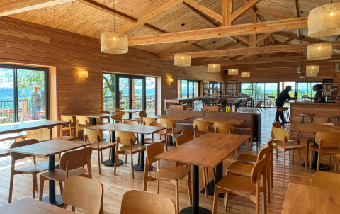 Interior de cafetería luminosa con muebles de madera en Village Huttopia Pays de Condrieu, Francia, vistas al bosque.