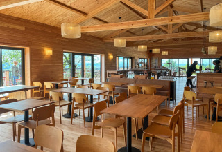 Heldere houten cafetaria met grote ramen in Village Huttopia Pays de Condrieu, Frankrijk, uitzicht natuur.