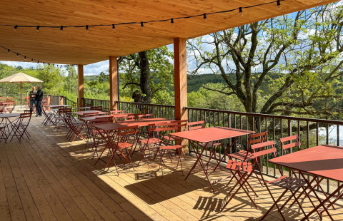 Terraza cubierta con mesas y sillas rojas con vistas a los árboles en Village Huttopia Pays de Condrieu, Francia.