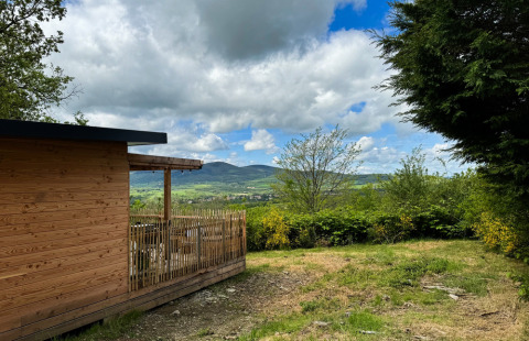 Wooden cabin with terrace overlooking green hills and mountains at Village Huttopia Pays de Condrieu, France.