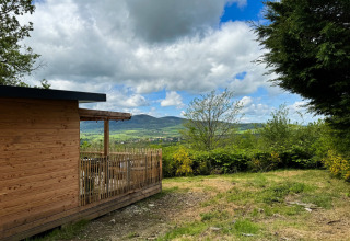Wooden cabin with terrace overlooking green hills and mountains at Village Huttopia Pays de Condrieu, France.