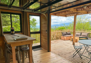 Wooden cabin with open deck and scenic mountain views at Village Huttopia Pays de Condrieu, France.