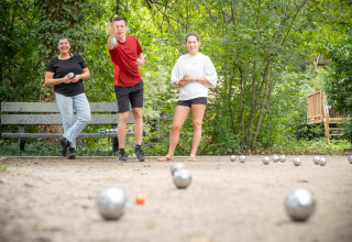 Drei junge Menschen spielen Boule im Freien im Ferienpark Village Huttopia Pays de Condrieu, Frankreich.