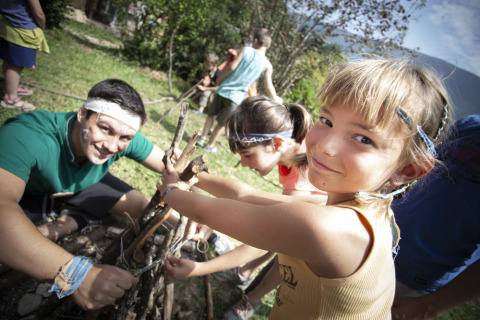 Des enfants et un adulte construisent un feu de camp avec des branches dans un parc de vacances en Auvergne-Rhône-Alpes.