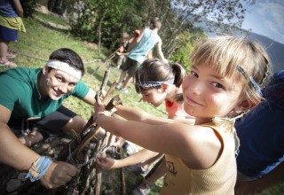 Des enfants et un adulte construisent un feu de camp avec des branches dans un parc de vacances en Auvergne-Rhône-Alpes.