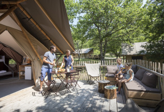 Familie nyder morgenmad på en træterrasse foran luksustelt i Village Huttopia Pays de Condrieu, Frankrig.