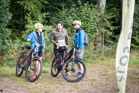 Trois personnes discutent avec des vélos au Village Huttopia Pays de Condrieu dans une forêt verdoyante.
