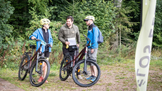 Tres personas con bicicletas conversando en el parque vacacional Village Huttopia Pays de Condrieu.