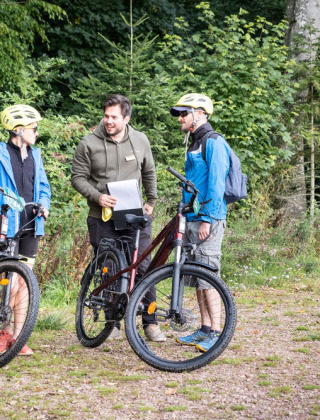 Drei Menschen mit Fahrrädern unterhalten sich in einem Ferienpark im grünen Wald in Frankreich.