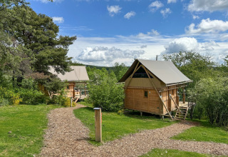 Two cozy wooden cabins surrounded by greenery at Village Huttopia Pays de Condrieu holiday park in France.