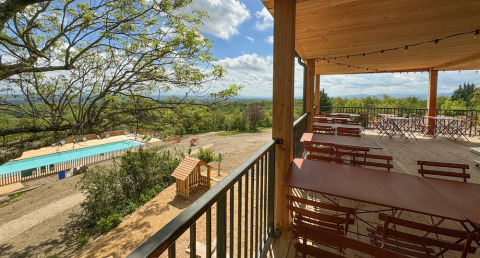 Terraza cubierta con mesas, vista a la piscina y naturaleza en Village Huttopia Pays de Condrieu, Francia.