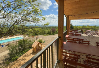 Covered terrace with tables, pool view, and greenery at Village Huttopia Pays de Condrieu holiday park in France.