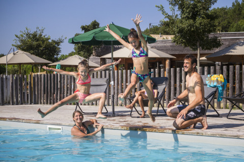 Familia divirtiéndose con niños saltando a la piscina en Village Huttopia Pays de Condrieu, Auvergne-Rhône-Alpes, Francia.