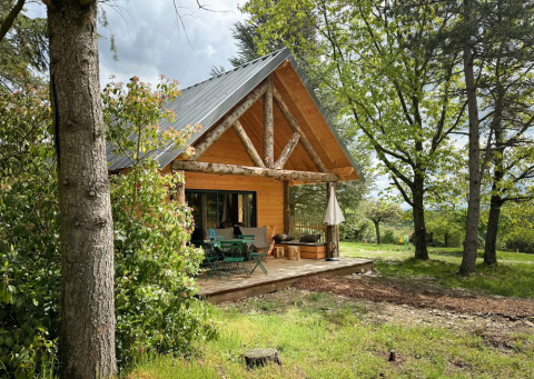 Cabaña de madera con terraza rodeada de árboles en Village Huttopia Pays de Condrieu, Auvernia-Ródano-Alpes, Francia.