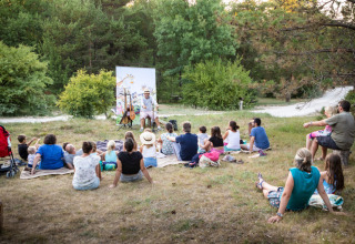 Udendørs underholdning med familier på tæpper, ser performer ved Village Huttopia Pays de Condrieu, Frankrig.