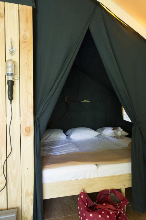Área de dormitorio acogedora en una tienda safari con cama doble, pared de madera y bolsa roja.