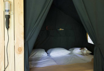 Cozy sleeping area inside a safari tent with a double bed, wooden wall, and red polka dot bag.