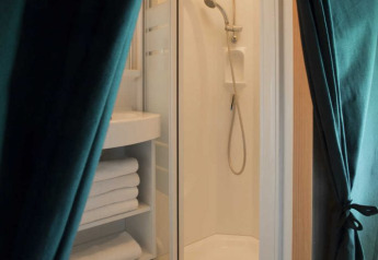 Shower cabin and towel shelves inside a safari tent with wood flooring and green curtains pulled aside.
