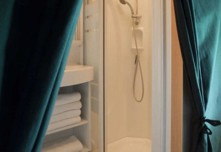 Ducha y estantería con toallas dentro de una tienda safari con suelo de madera y cortinas verdes abiertas.